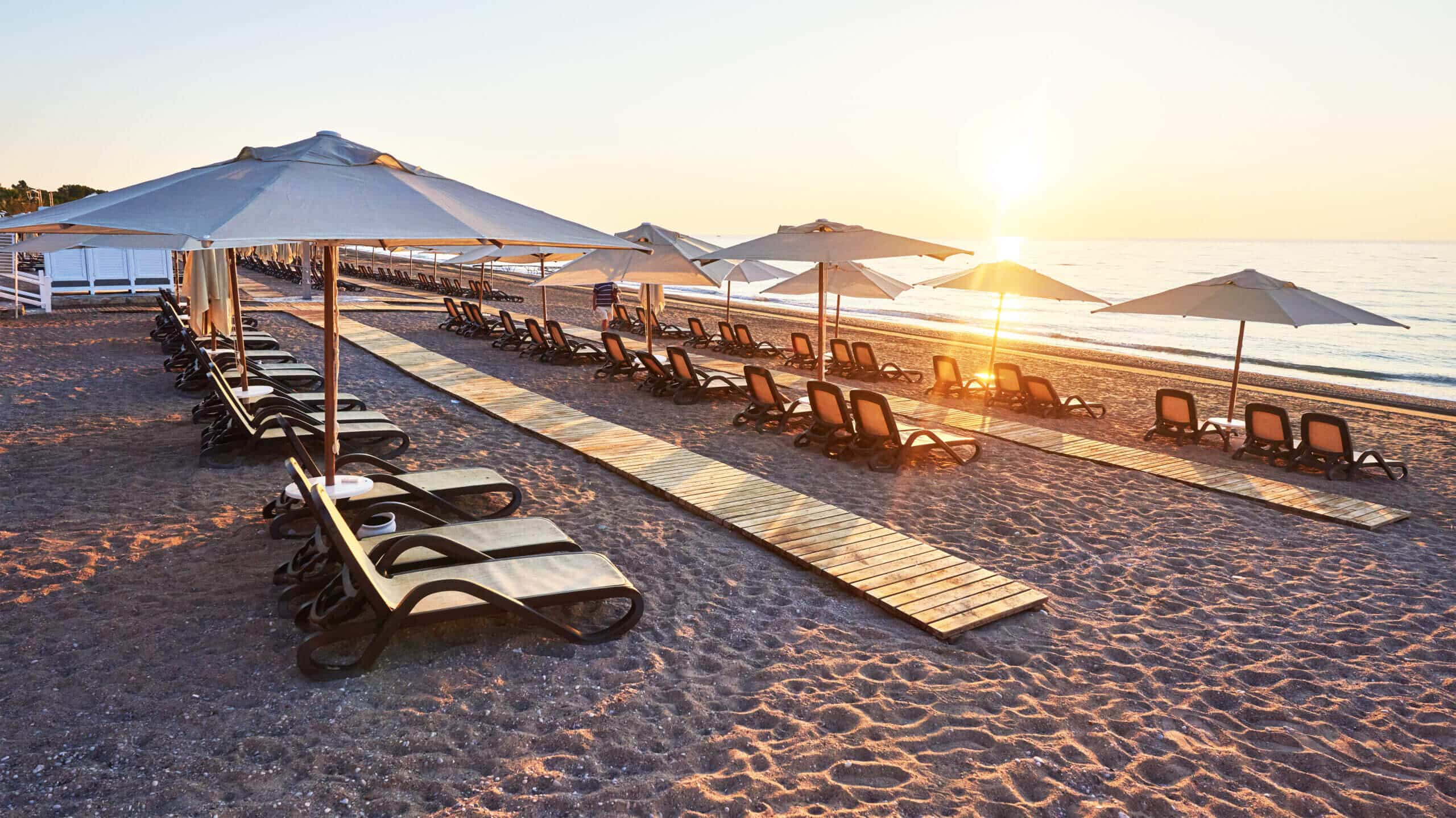 Strand mit Strandliegen, Sonnenschirmen und Sonnenuntergang